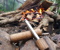 fire piston firemaker in front of campfire